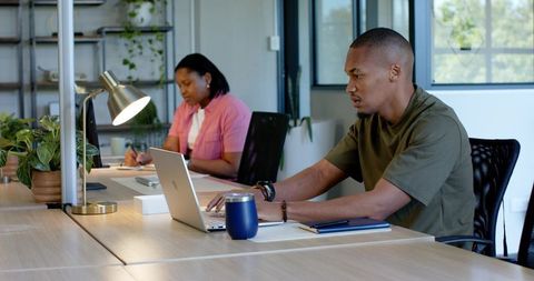 Focused coworkers collaborating at sunlit coworking desk, man typing, woman writing notes