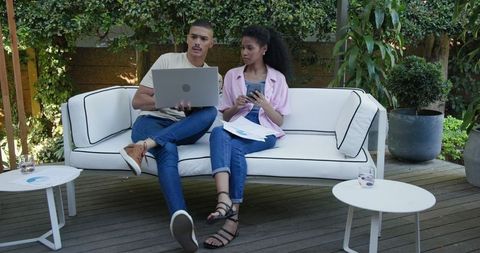 Diverse Couple Collaborating Outdoors Using Laptop and Smartphone
