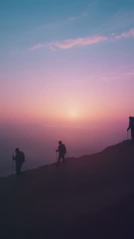 Hikers traversing mountain ridge at sunrise with backpacks and trekking poles
