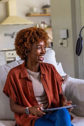 African american woman recording podcast at home with tablet and microphone, smiling