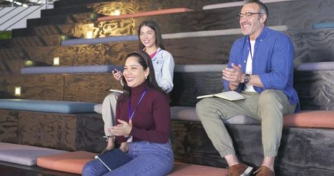 Applauding diverse colleagues sitting on tiered risers during modern workshop session