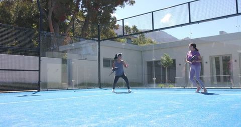 Active mature women playing padel on vibrant blue outdoor court under clear sky