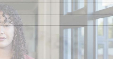 Curly-haired woman standing by modern glass windows in crimson blouse with copy space