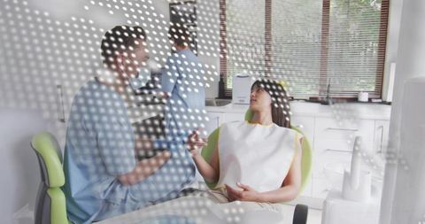 Dentist consulting patient reclining in green dental chair wearing mask and bib