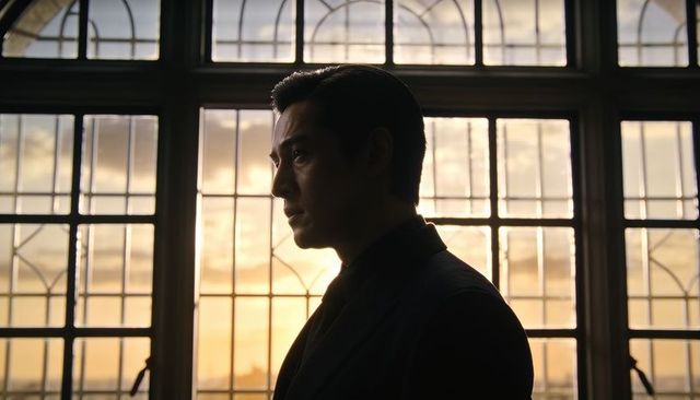 Contemplative silhouetted asian man in dark suit standing by arched leaded window at sunset