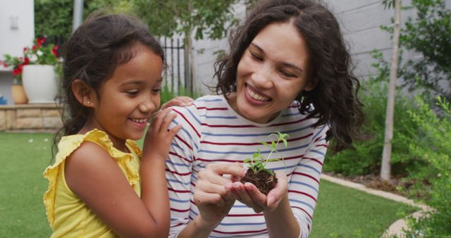 Smiling woman and young girl planting a seedling together in a garden, highlighting family bonding and environmental education. Ideal for content related to gardening, nature, sustainability, family activities, parenting, and environmental awareness.