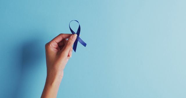 Image of hands of caucasian woman holding blue ribbon on blue background. medicine, health, cancer awareness concept digitally generated image.