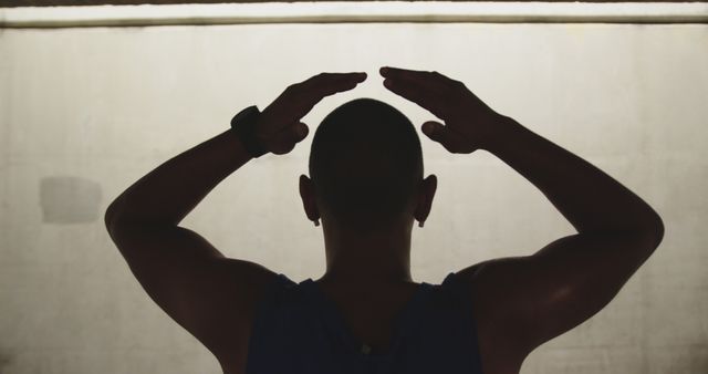 A silhouette of a biracial man putting his hands on his head, resting, wearing sportswear, view from behind. Sports and working out.