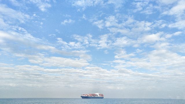 Large cargo ship sailing on open sea under cloudy sky. Useful for transportation, shipping, and logistics themes. Great for articles about global commerce, freight services, and maritime travel. Can also illustrate import/export businesses, sea adventures, and scenic seascapes.