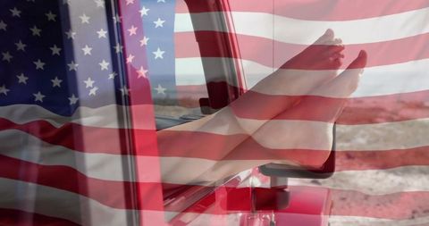 Bare legs stretching from red truck window with american flag overlay evoking road trip freedom
