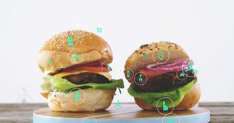 Two gourmet burgers sitting on round wooden board with teal energy icons overlay