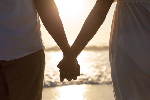 Mid section of couple standing together hand in hand on the beach