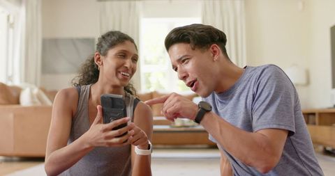 African couple sharing fitness device and laughing in bright minimal living room