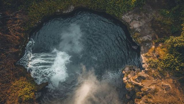 Aerial view showing circular plunge pool with dark swirling water, foamy inflow and mist