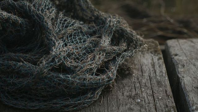 Fraying fishing net resting on weathered dock planks coastal close-up texture and fibers