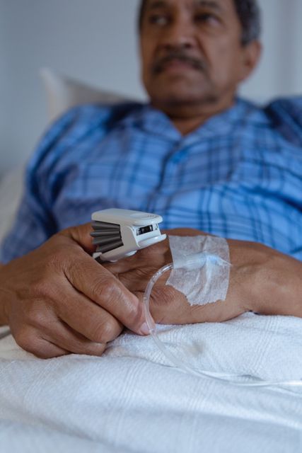Mature male patient lying in hospital bed receiving medical treatment. He has an IV drip in his hand and a pulse oximeter on his finger. This image can be used for healthcare, medical care, patient recovery, and hospital-related content.