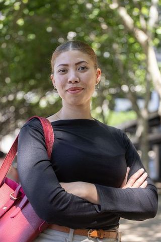 Confident woman in twenties standing on sunlit path carrying pink tote and hoop earrings