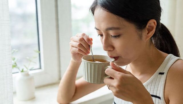Morning tea ritual: woman stirring steaming mug by sunlit window, enjoying calm moment