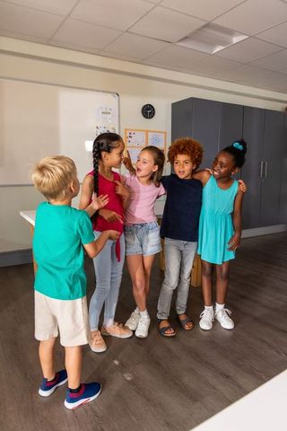 Elementary students chatting and laughing in classroom forming friendly diverse friendship circle