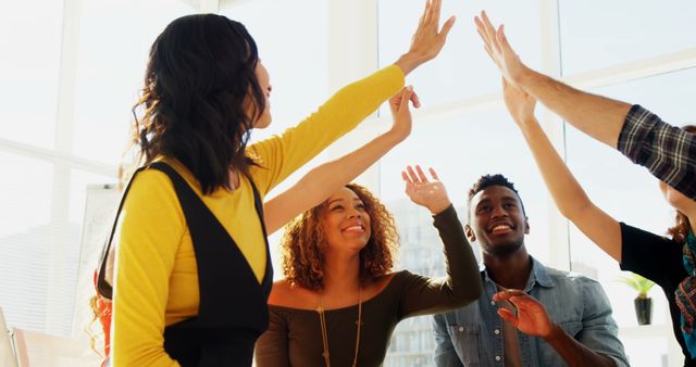 A diverse group of young adults is celebrating with high-fives in a bright room, with copy space - Download Free Stock Photos Pikwizard.com