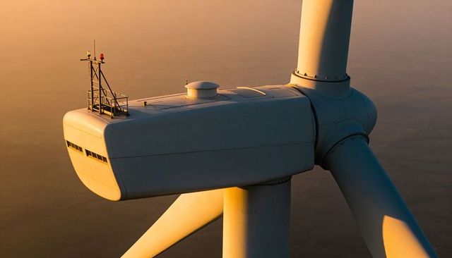Offshore wind turbine nacelle and rotor at golden hour over calm sea, renewable energy