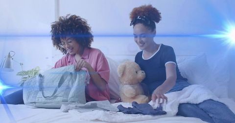 Young friends unpacking weekend duffel on cozy bed with teddy bear