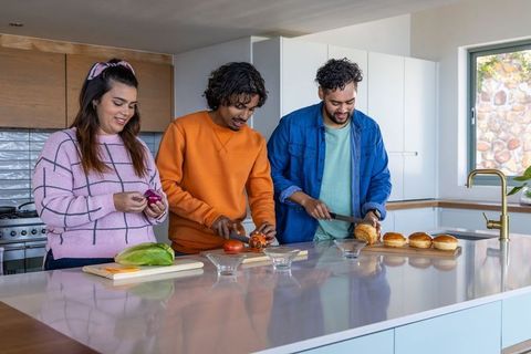 Friends preparing gourmet burgers on glossy kitchen island chopping fresh ingredients