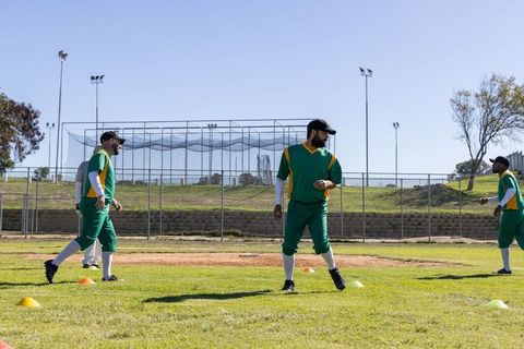 Asian baseball teammates practicing fielding drill in green and yellow uniforms on grass