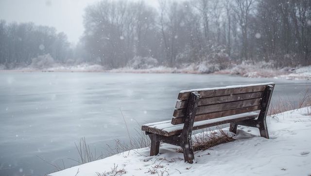 Snow-covered bench facing frozen lake on quiet winter shoreline