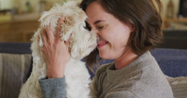 Smiling caucasian woman kissing and cuddling her pet dog sitting on sofa at home. lifestyle, pet, companionship and animal friendship concept.