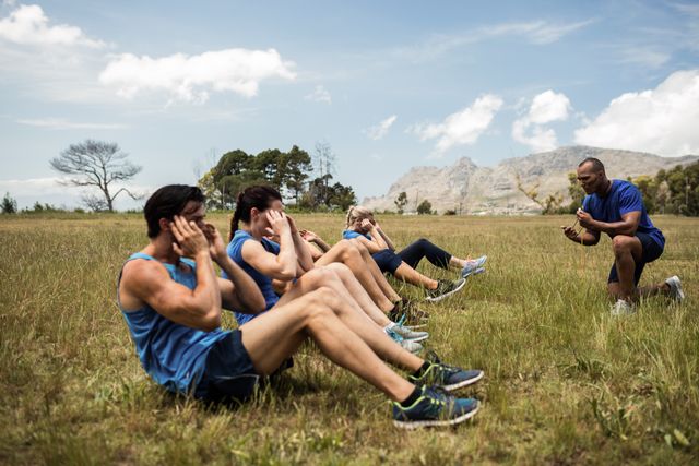 Group of fit individuals performing crunches in an outdoor bootcamp with a personal trainer guiding them. Ideal for promoting fitness programs, outdoor exercise routines, and healthy lifestyle campaigns. Can be used in advertisements for gyms, fitness classes, and personal training services.