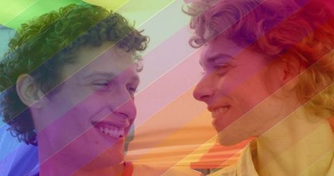 Two men smiling face-to-face at waterfront rainbow overlay celebrating love and pride