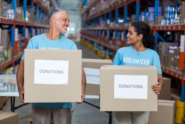 Happy volunteers are holding donations boxes and looking each other in a warehouse