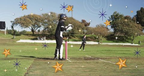 Female wicket-keeper standing behind pink stumps on grassy cricket pitch in sunny match