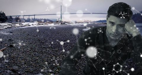 Pensive Man on Scenic Pebble Beach with Futuristic Overlay