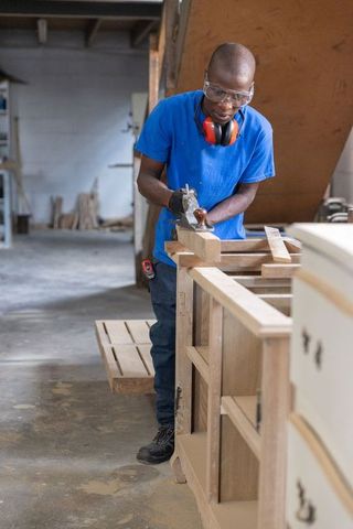Smoothing wooden cabinet panel with hand plane in workshop, artisan woodworking craft