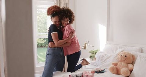 Two African American Women Embracing in Sunlit Bedroom Showing Affection and Connection