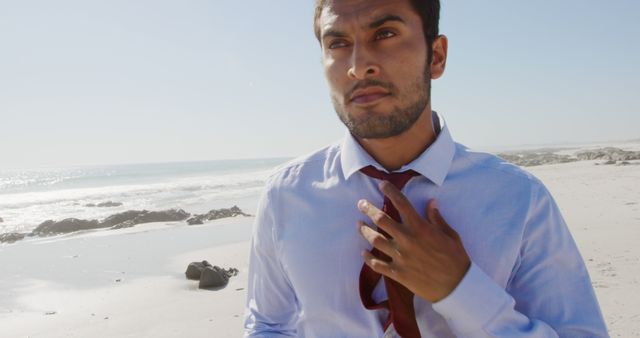 Man in business attire on beachfront relaxing and loosening tie, embodies modern work-life balance. Ideal for use in articles about stress relief, professional retreats, corporate wellness, and vacation ideas for busy professionals. Symbolizes career-oriented relaxation and taking a break from the hustle.