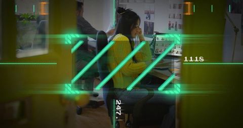 Young woman in yellow sweater working at open-plan studio desk with neon green hud overlay
