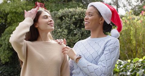 Friends celebrating holiday in garden wearing santa hat and merry headband in cozy sweaters