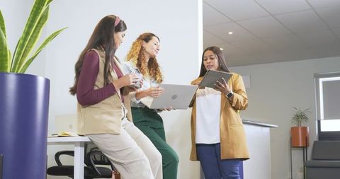 Multicultural women collaborating at modern office reception with laptop and tablet