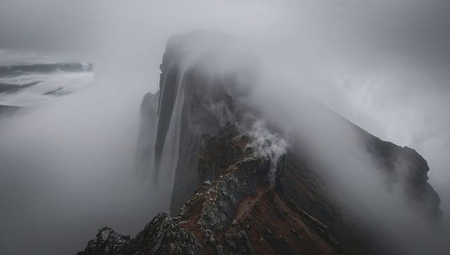 Fog-hugging jagged coastal ridge with narrow trail and misty cliffs, crashing waves