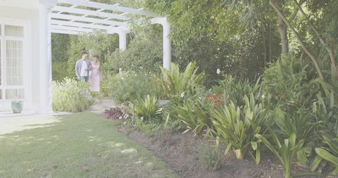 Couple walking through lush garden pergola along sunlit path with romantic atmosphere