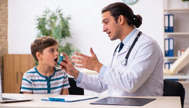 Pediatrician teaching inhaler technique to boy at clinic with compassionate guidance