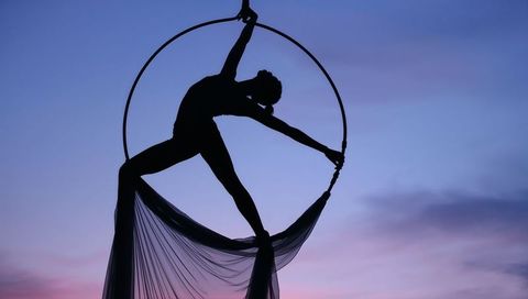 Silhouette aerialist on lyra hoop at dusk with flowing silk drapery