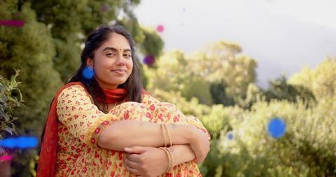 Indian woman sitting in garden hugging knees wearing floral kurta red dupatta serene smile