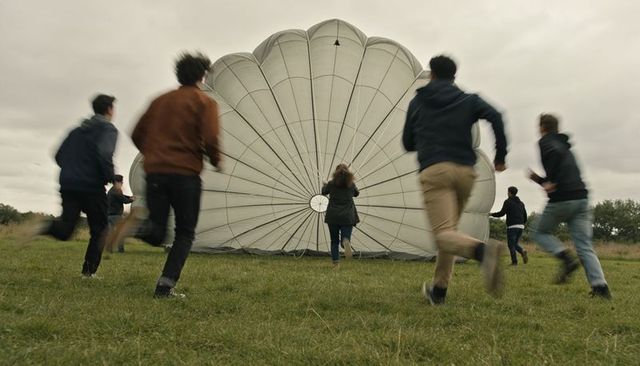Group rushing toward inflated parachute canopy on grassy meadow, dynamic motion and teamwork