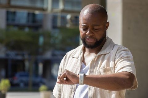 African american man checking smartwatch on sunny urban street near modern apartments