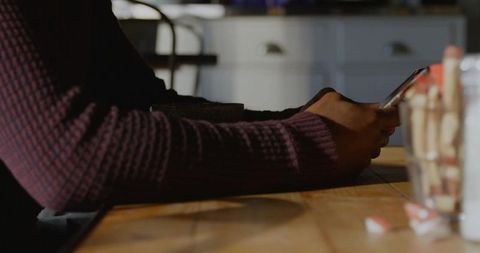 Person in burgundy sweater using smartphone at rustic cafe