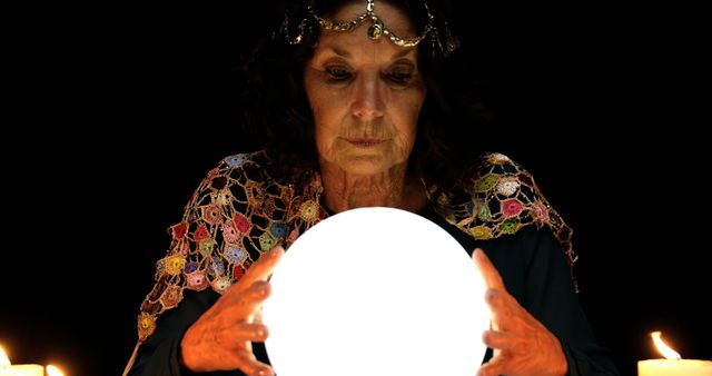 A middle-aged Caucasian woman gazes intently into a crystal ball, surrounded by candles, suggesting a mystical or fortune-telling theme. Her focused expression and the ambient lighting create a sense of intrigue and mystery.